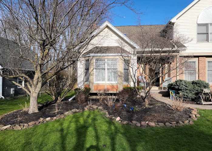 Single-story home with tan siding, brick accents, bay window, and bare trees in front yard