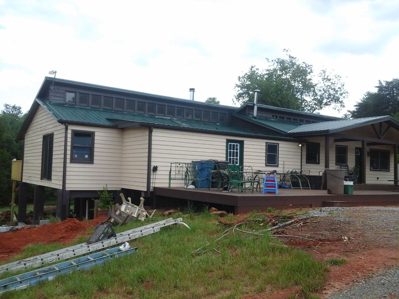 Elevated residential home with cream siding, green metal roof, and front deck with construction materials