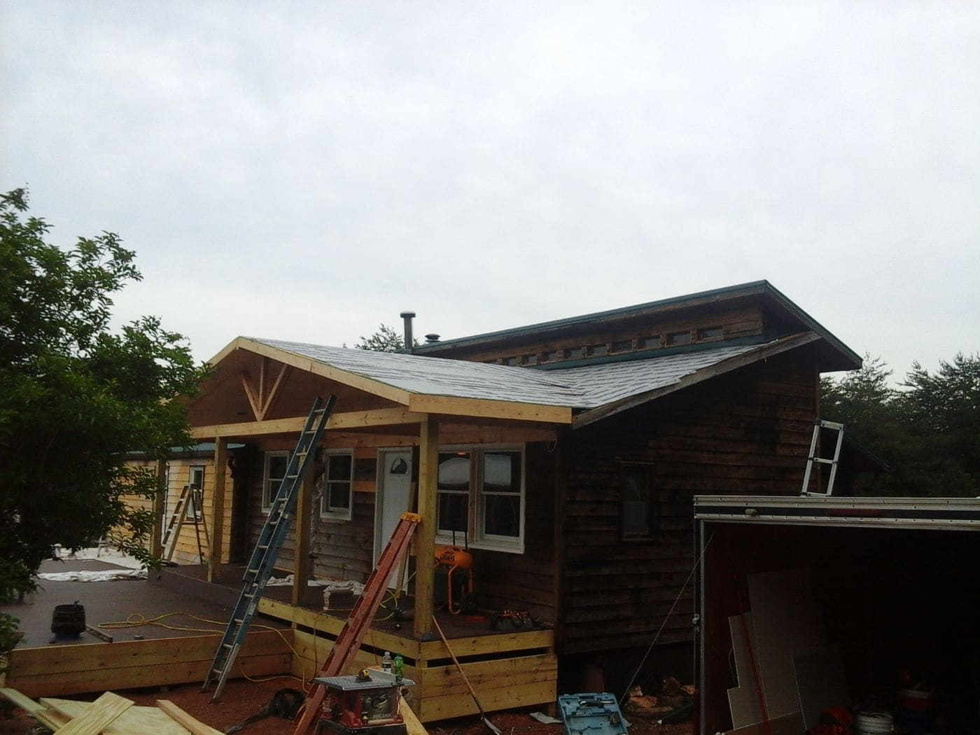 Wooden house under construction with metal roof, ladders, and tools on overcast day
