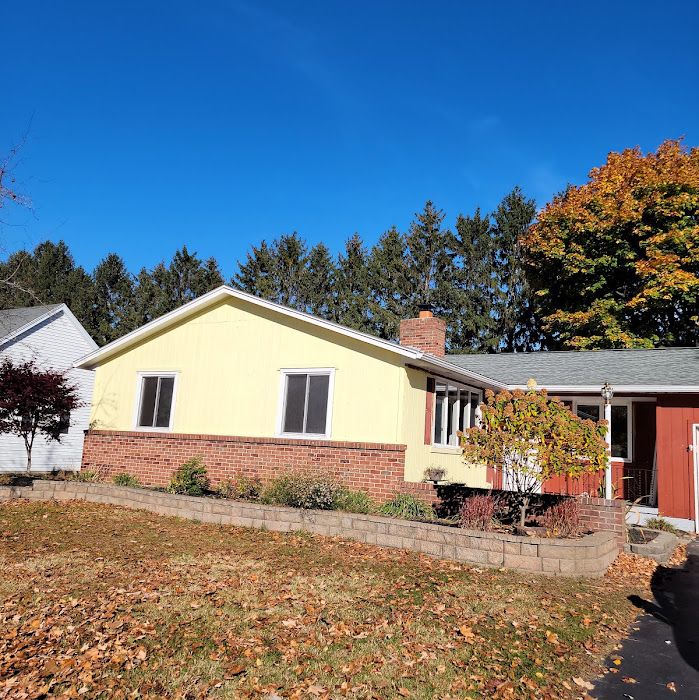 Yellow and brick ranch house with red door on autumn day with bare lawn