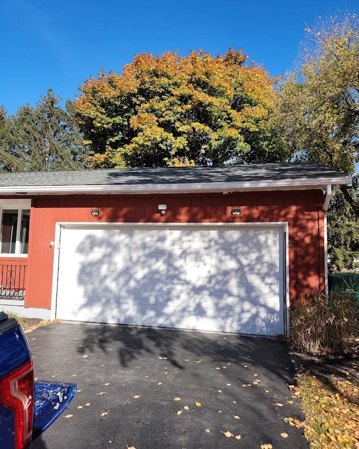 Red residential home with white garage door and autumn foliage in background