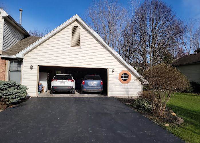 Two-car garage with white siding and two vehicles parked inside on a residential driveway
