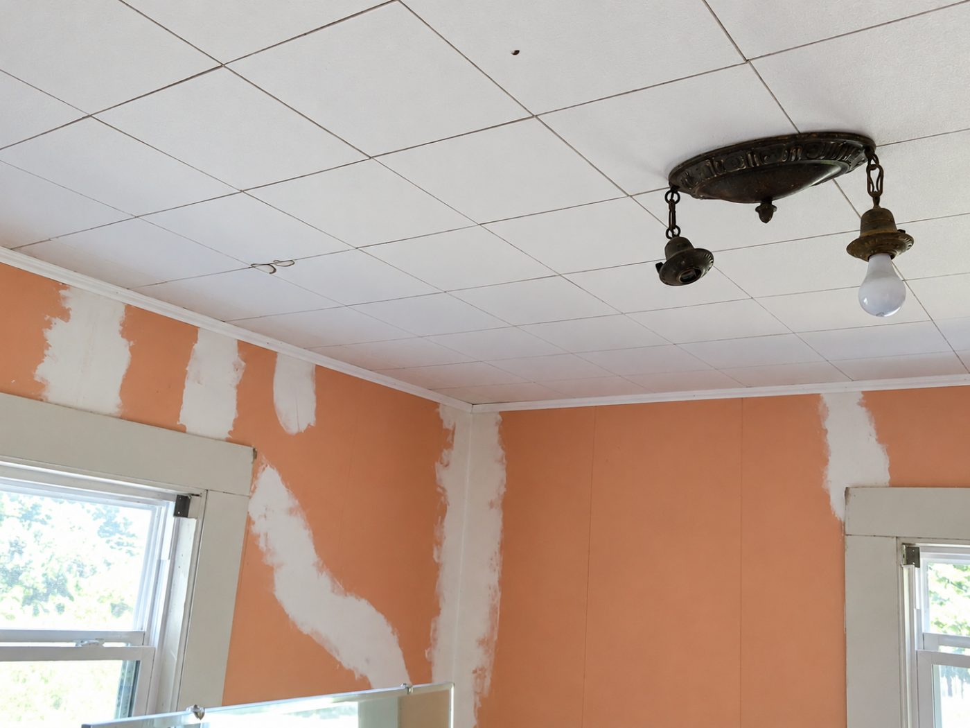 Interior room with orange walls being painted, drop ceiling, and brass light fixture with bulb