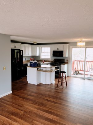 Modern kitchen with white cabinetry, black appliances, island with seating, and hardwood floors