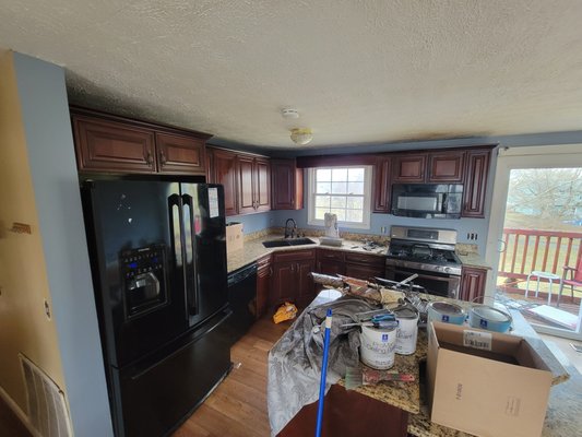 Kitchen renovation in progress with dark cabinets, black appliances, and construction materials on countertop