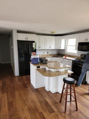 Modern kitchen with white cabinets, granite countertop island, black appliances and wood flooring