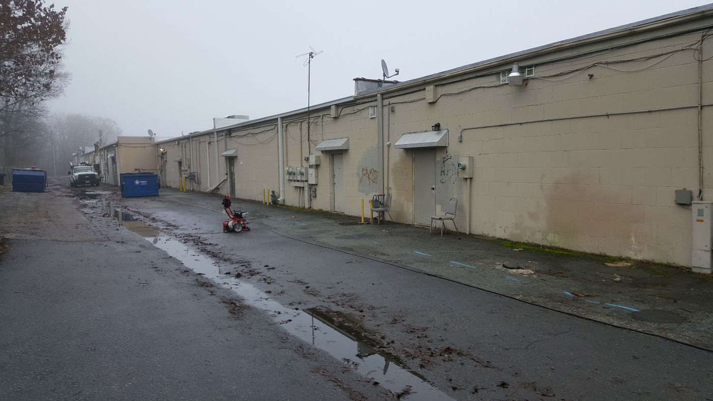 Industrial facility with tan buildings, wet pavement, and parked equipment on overcast day