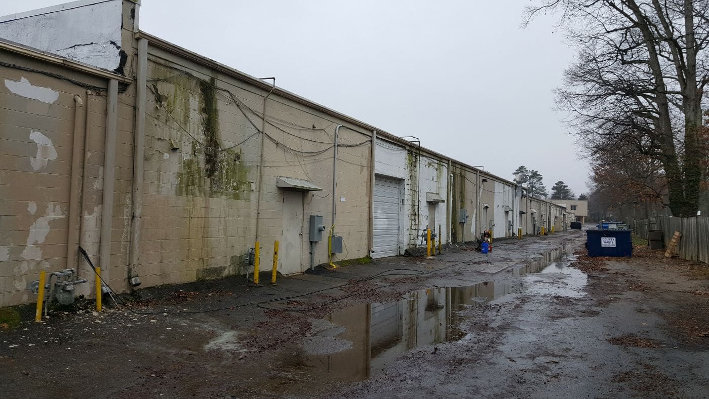 Row of industrial warehouse units with metal doors and yellow bollards along wet pavement