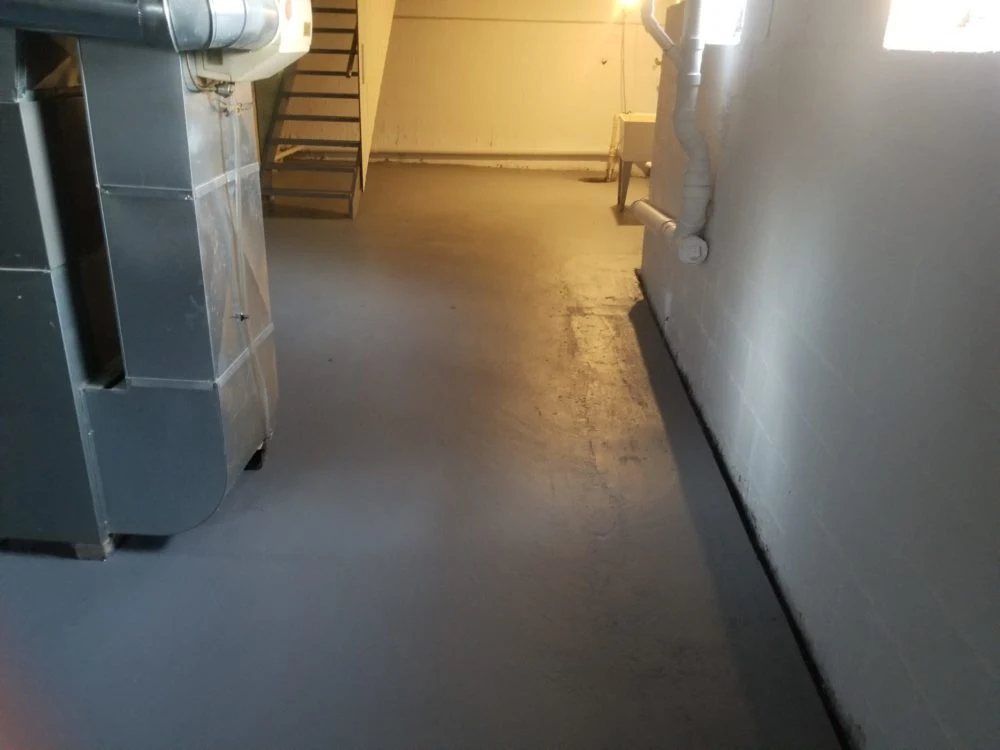 Industrial basement corridor with concrete floor, metal ducts, and staircase