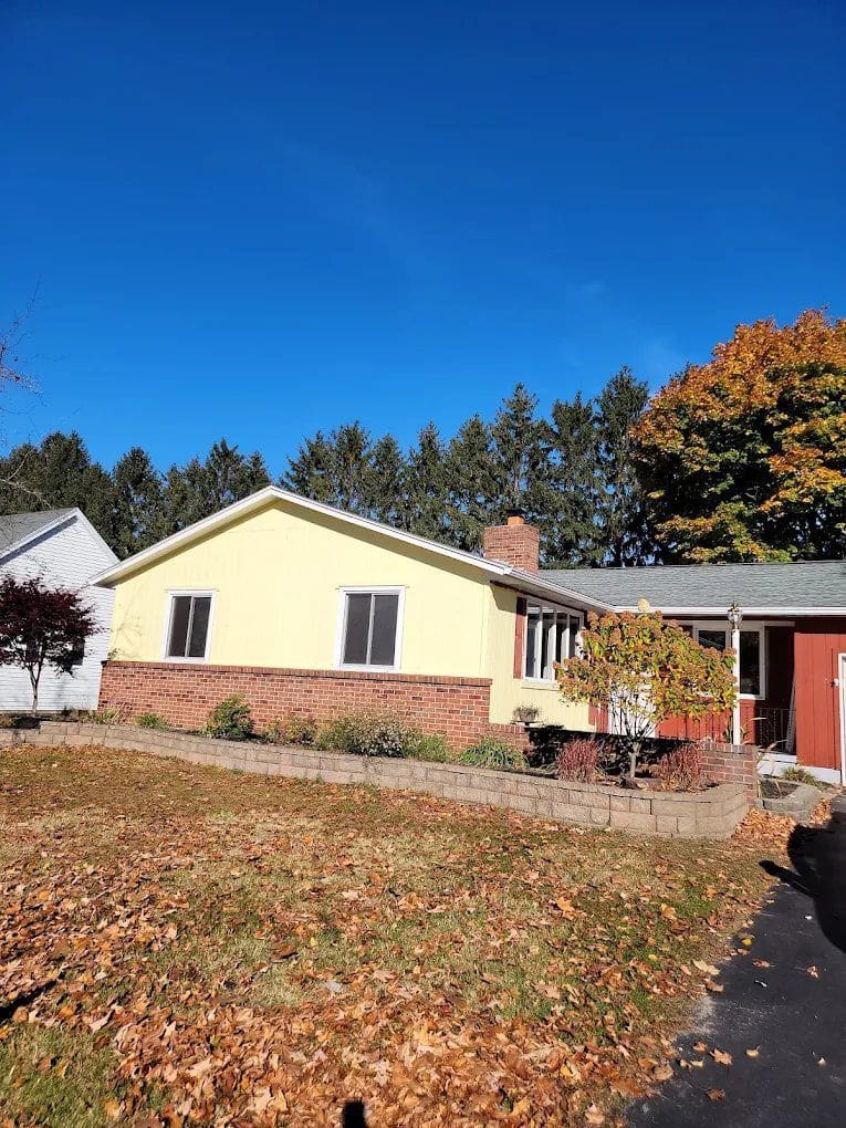 Yellow and brick ranch-style home with red door and attached garage on autumn day