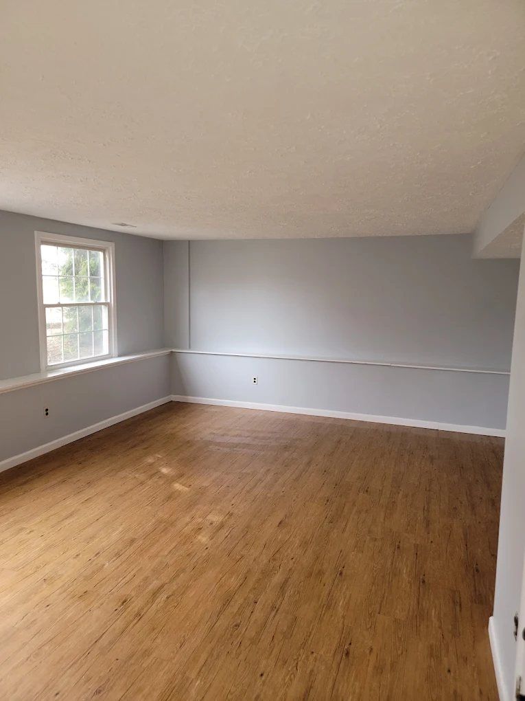 Empty room with wood flooring, white walls, textured ceiling, and window with natural light