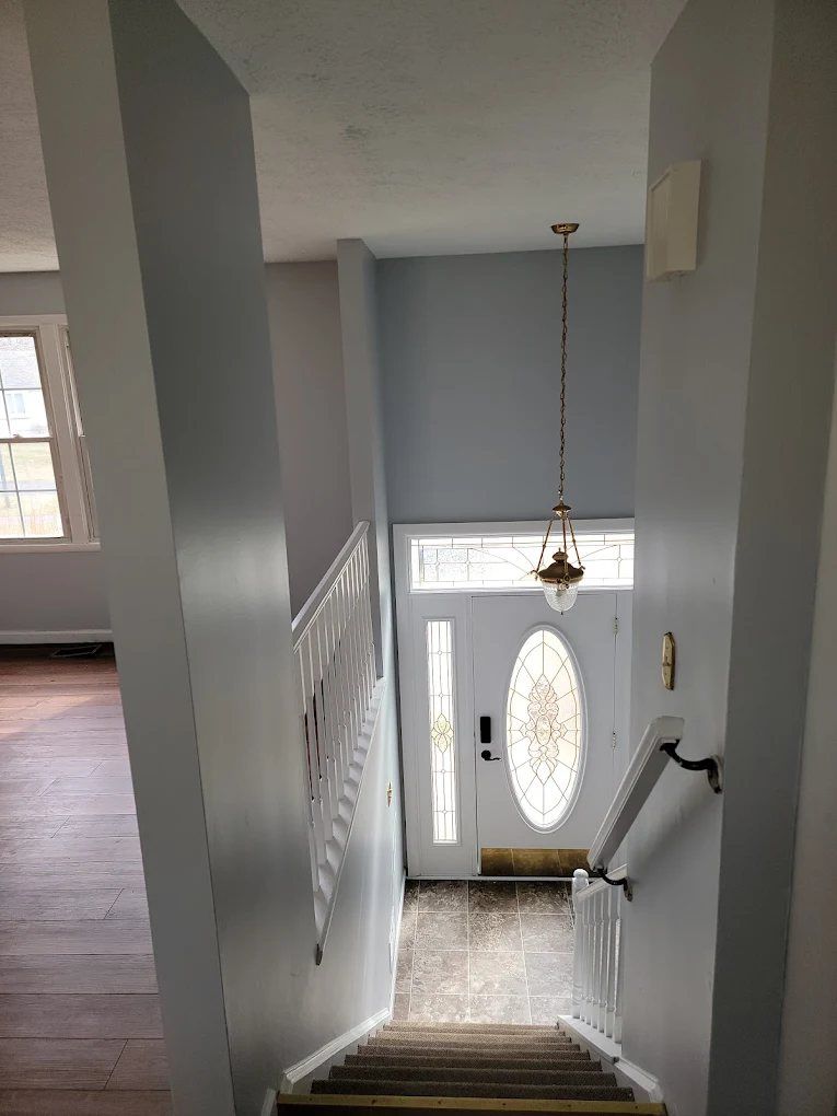 Bright entryway with white walls, staircase, ornate oval door with transom window, and pendant light fixture